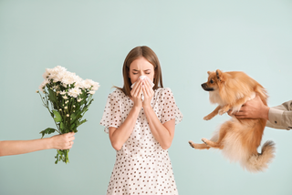 women sneezing while dog and flowers are held next to her