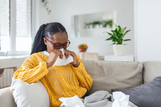 women on couch sneezing holding a tissue to face