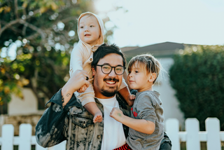 photo of a family with a man and his son on his shoulder while holding the other son on a neighborhood street