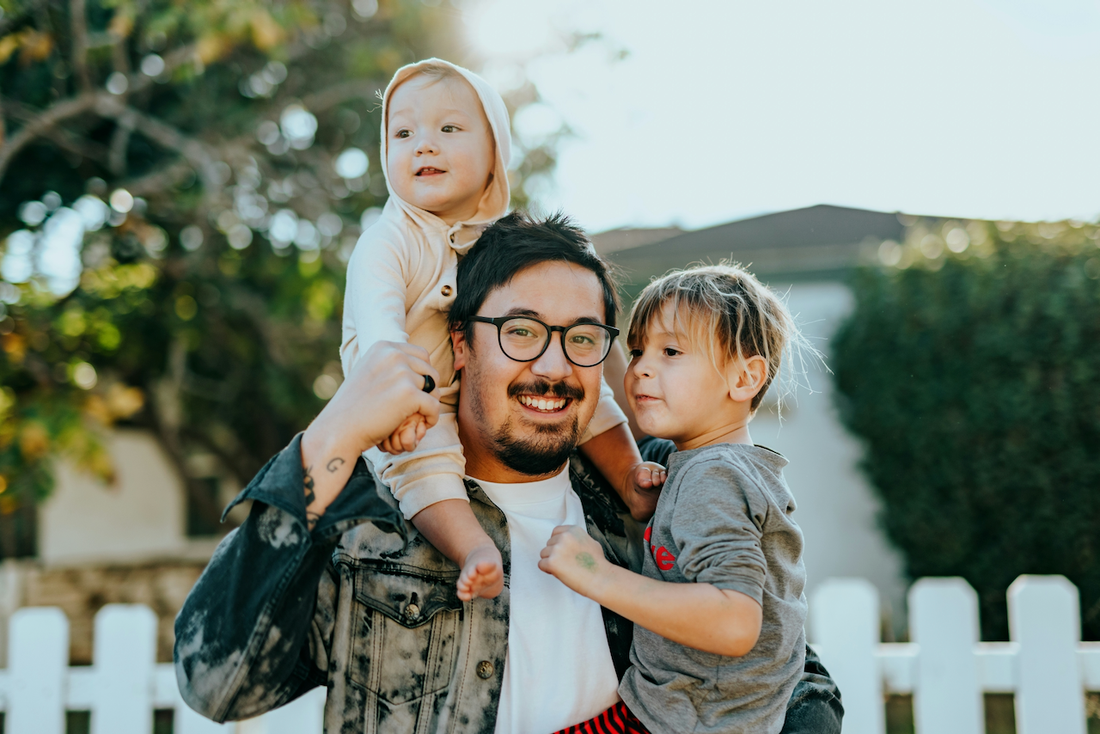 photo of a family with a man and his son on his shoulder while holding the other son on a neighborhood street