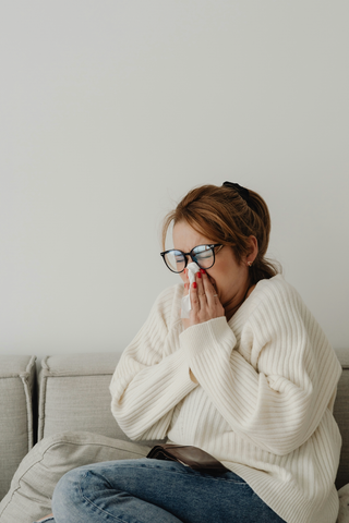 women wearing white sweater sitting on couch sneezing