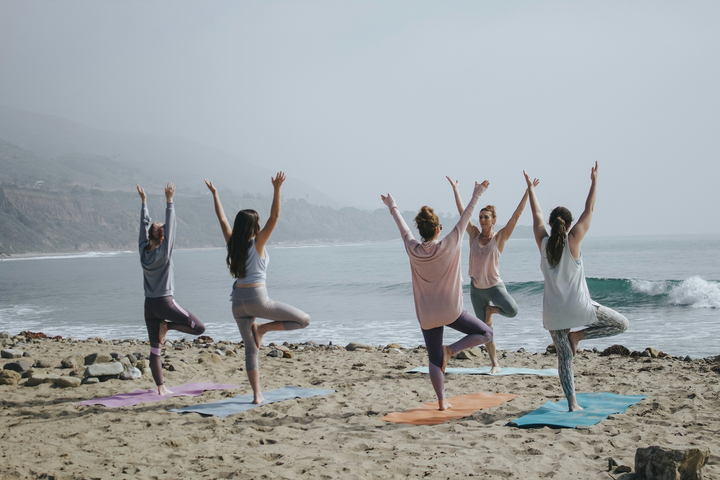 a group of women doing yoga outside by the beach