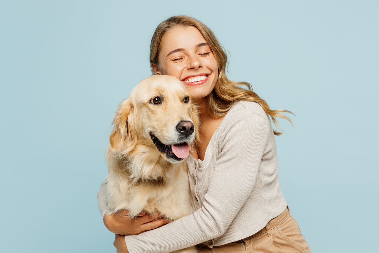 Woman holding a golden retriever against a light blue background