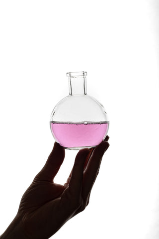hand holding glass bottle with light pink soapy liquid on white background