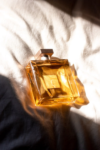 perfume bottle laying on section of bed with white sheets and shadows