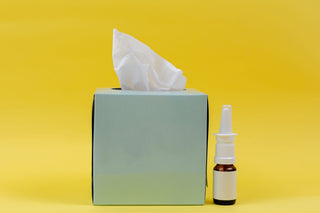 tissue box next to nasal spray allergy meds on yellow background