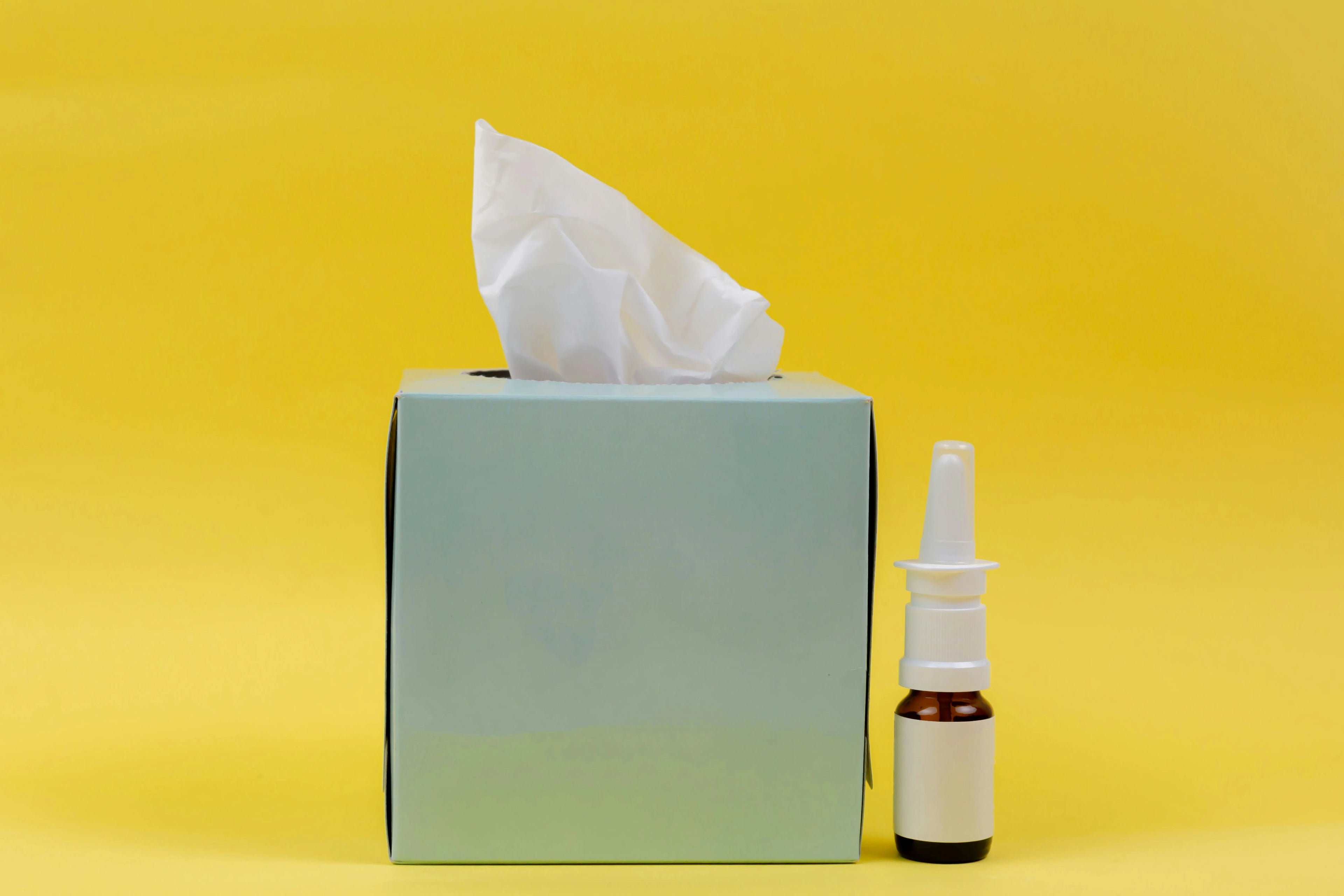 Tissue box and nasal spray bottle on a yellow background