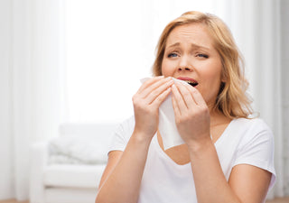 women holding tissue to face about to sneeze in front of white couch