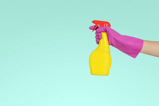 person wearing pink glove holding yellow spray bottle on light blue background